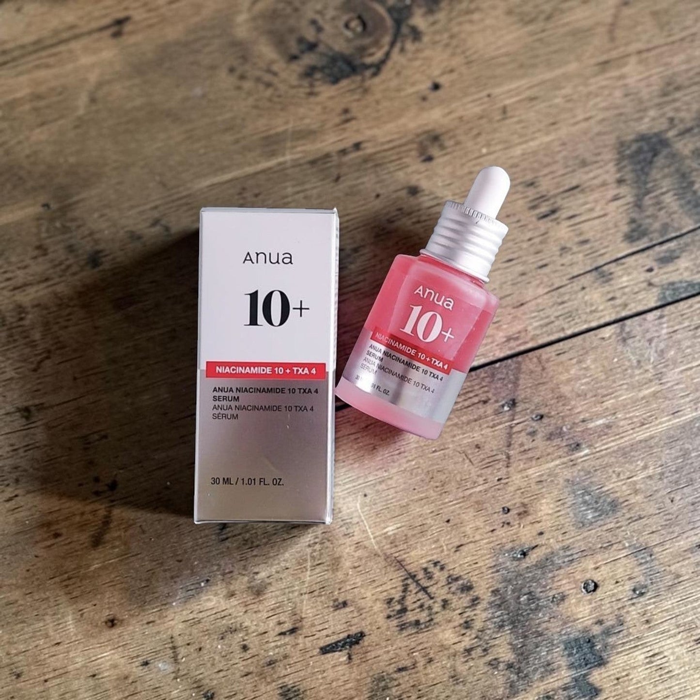 Anua Niacinamide 10% + TXA 4% Serum in a pink glass bottle with a dropper, 30ml. The serum box is white and grey.